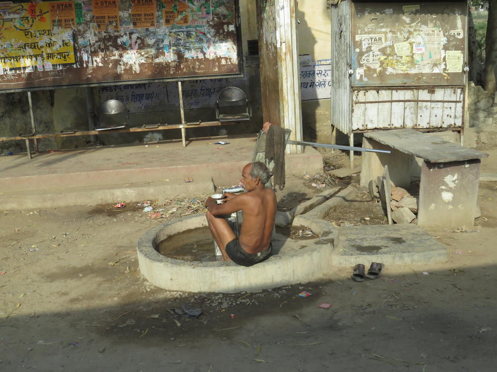 A man bathing near a small water pump, a common scene, Rajasthan
